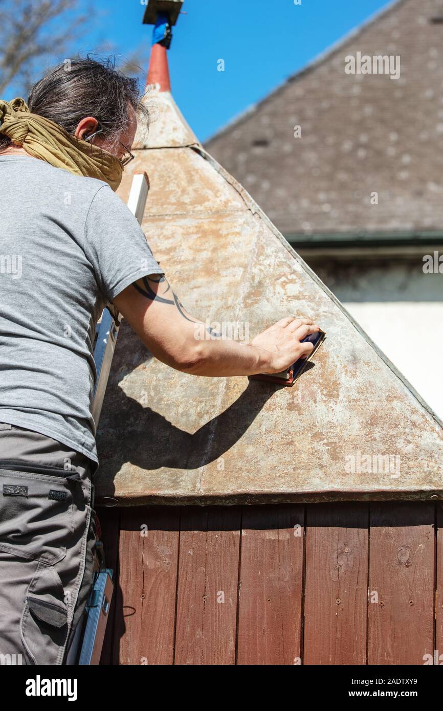 Man sanding the tin roof of his backyard shed with a sanding block, removing rust and dirt Stock Photo