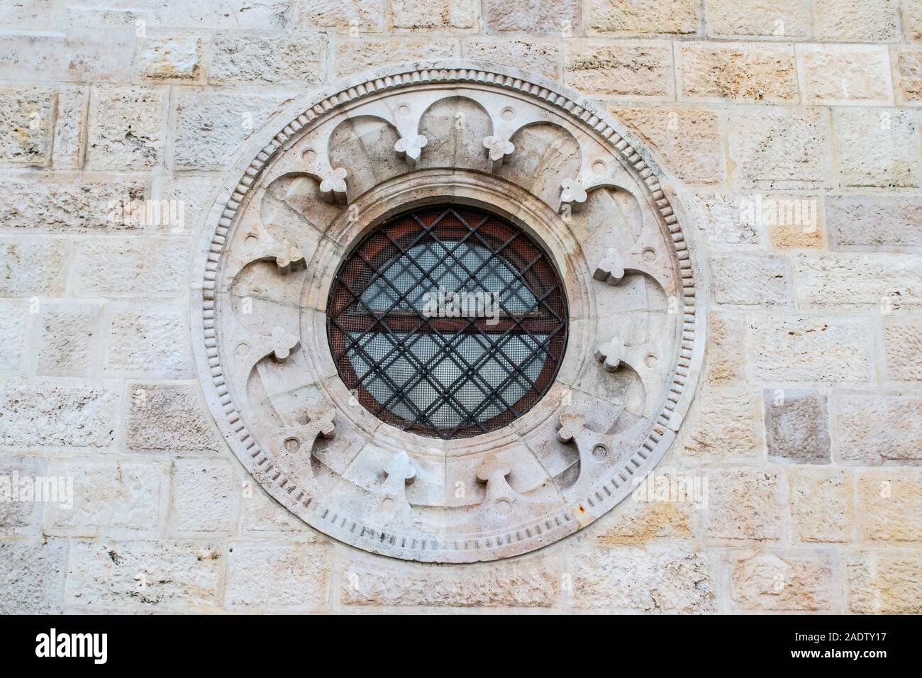 Round window with a black metal fence and a pattern in an old brick and stone facade Stock Photo