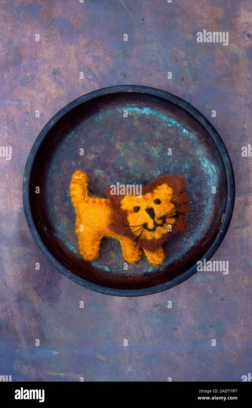 Felt model of lion with smiley face in tarnished copper dish Stock Photo