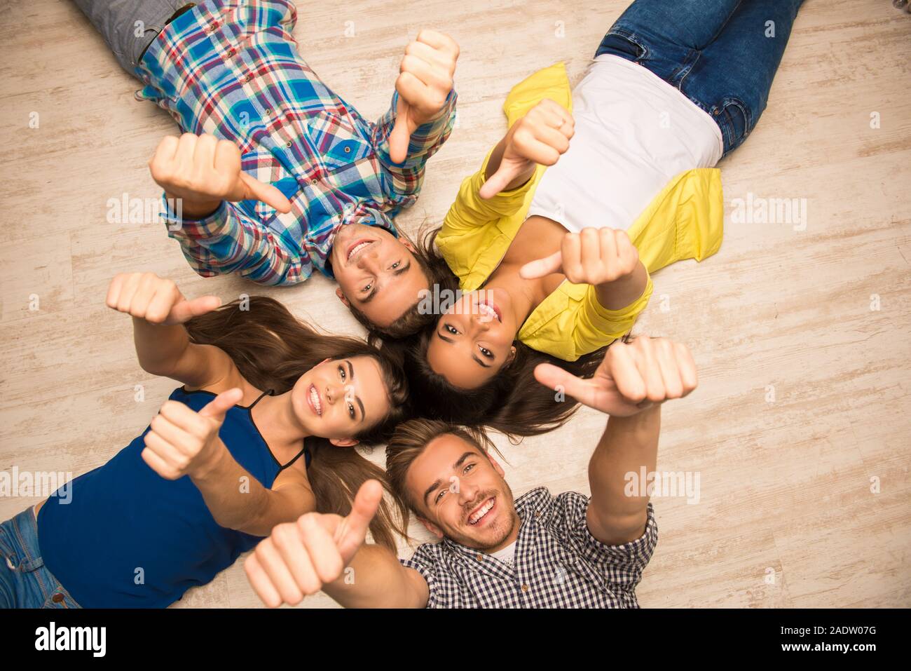 Cheerful Young People Lying On The Floor Showing Thumbs Up Stock