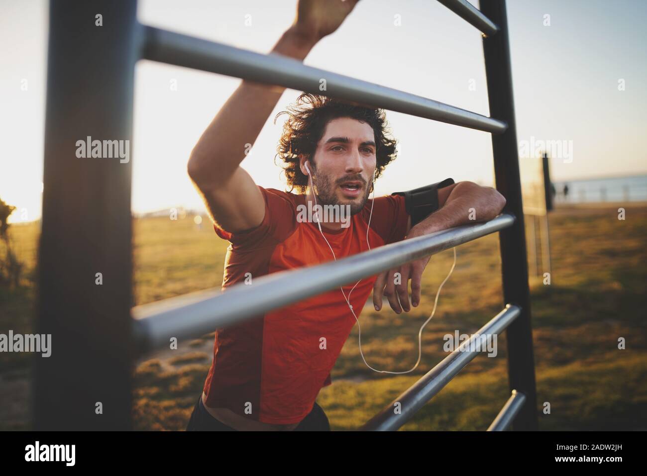 Young athletic man taking a break from training standing with hands on vertical bars at outdoor gym park in the morning Stock Photo