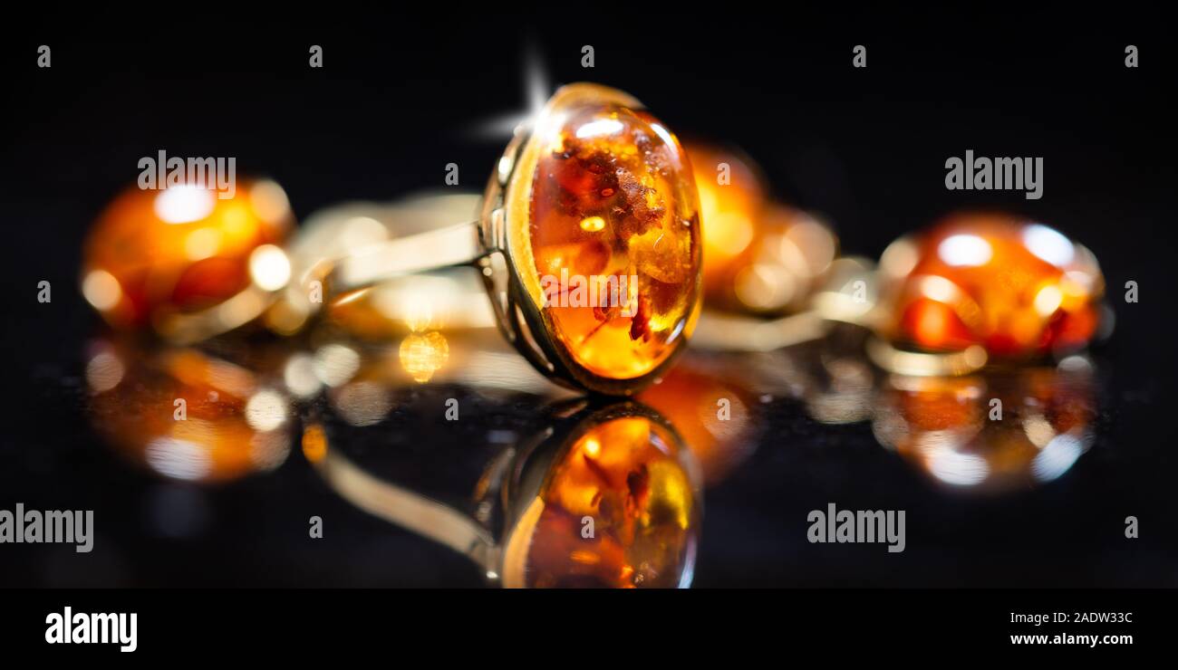 panorama of jewelry with amber stones, amber necklace ring and earring and pendant with noble metal like gold, in front of a black background on a bla Stock Photo