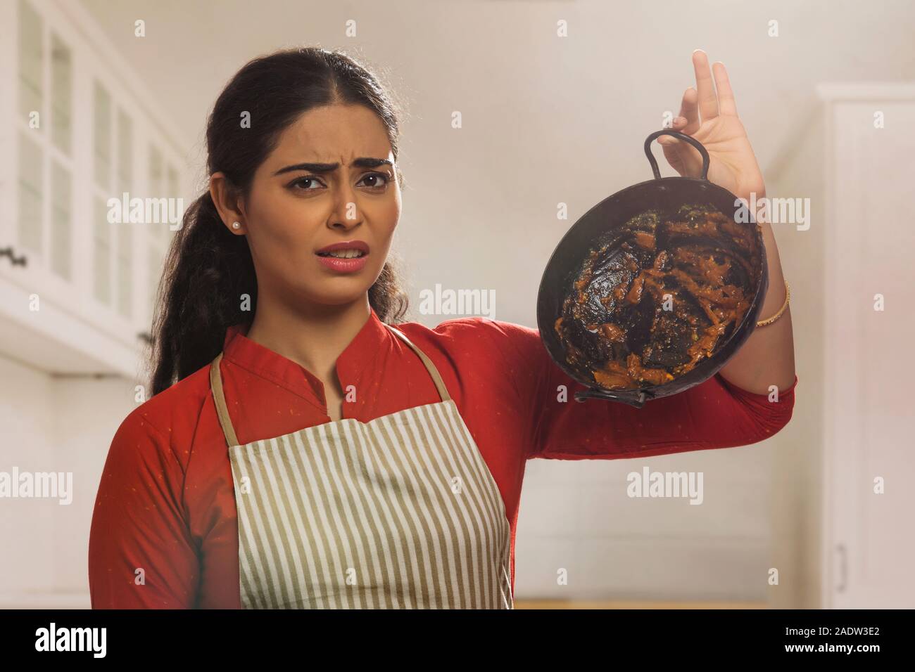 Portrait of a single woman wearing an apron and holding dirty utensil in hand. Stock Photo