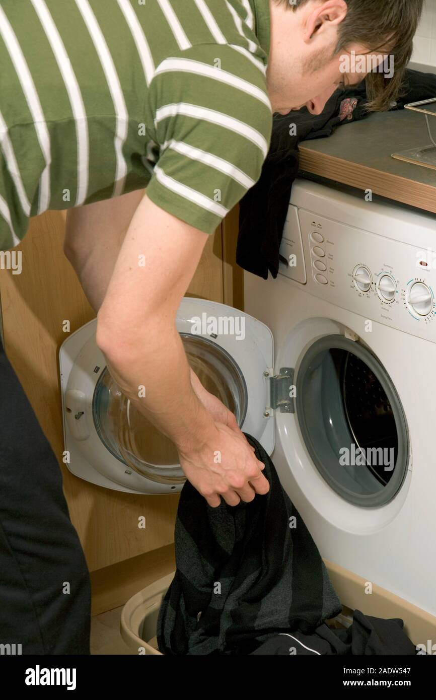 Young man putting laundry in washing machine, close-up, side view Stock Photo