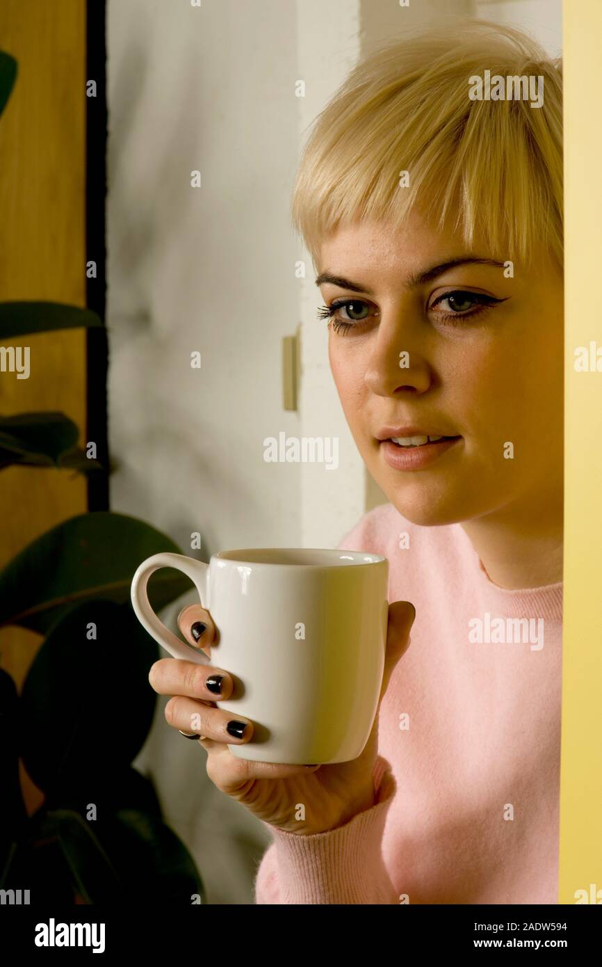 A young woman, 20's,  sitting on a kitchen worktop drinking coffee Stock Photo
