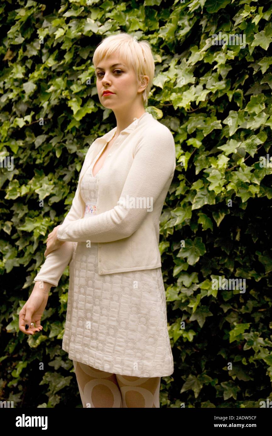 A stylish young woman standing with attitude in front of an ivy covered wall background Stock Photo