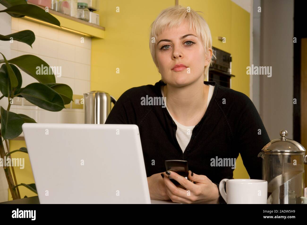 A young woman working from home in her kitchen laptop open on the table in front of her. Stock Photo
