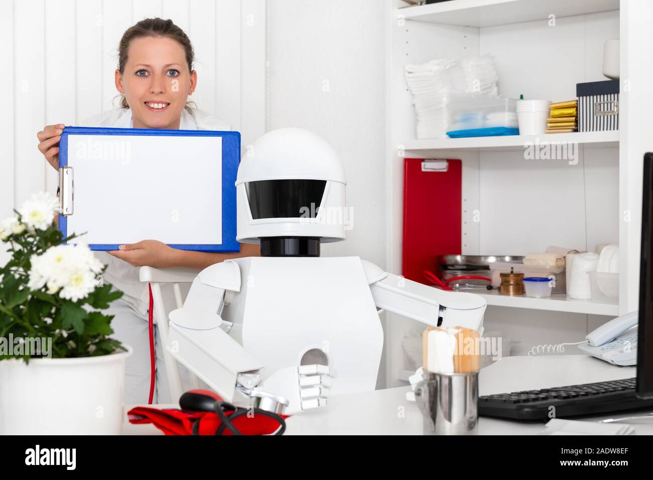 ai robot as professional doctor in his office, sitting behind the desktop, nurse or second female doctor with clipboard in her hands Stock Photo