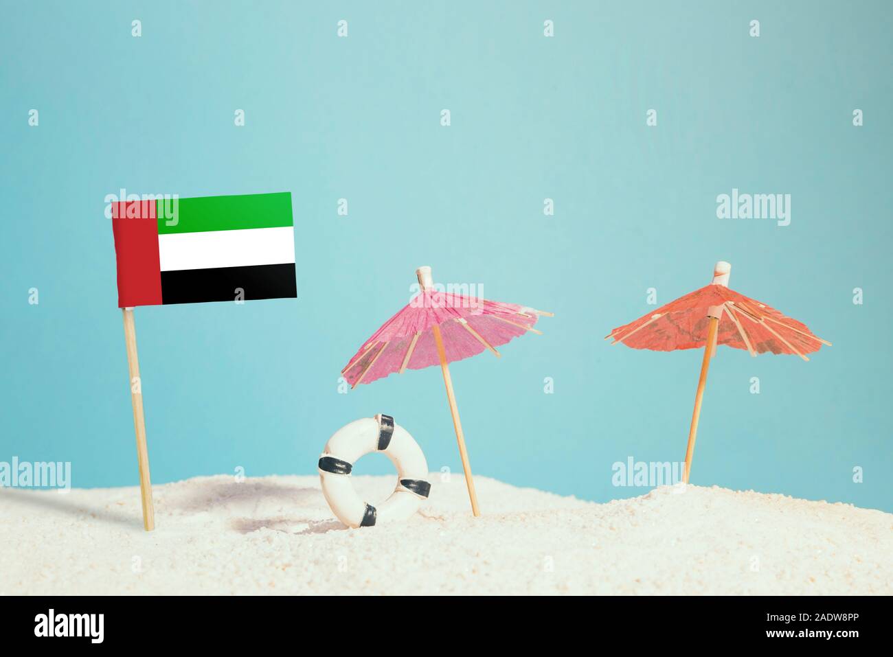 Miniature flag of United Arab Emirates on beach with colorful umbrellas and life preserver. Travel concept, summer theme. Stock Photo