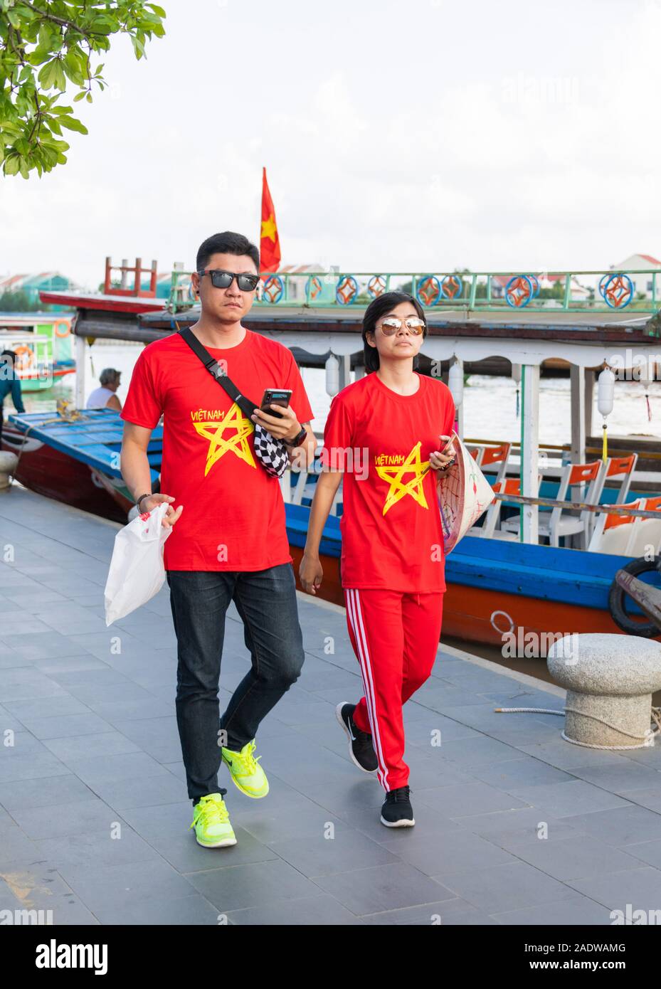 Tourists wearing matching red Vietnam T shirts walking along riverfront Hoi An Vietnam Stock Photo