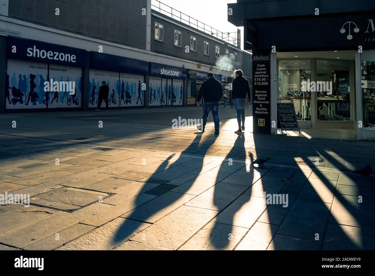 Smokers walking into early morning sunshine in Basildon Town centre in Essex. Stock Photo