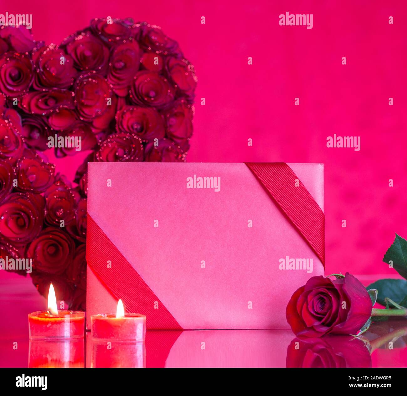 Closeup of a blank Valentine card and red roses with burning candles on a reflective tabletop with copy space Stock Photo