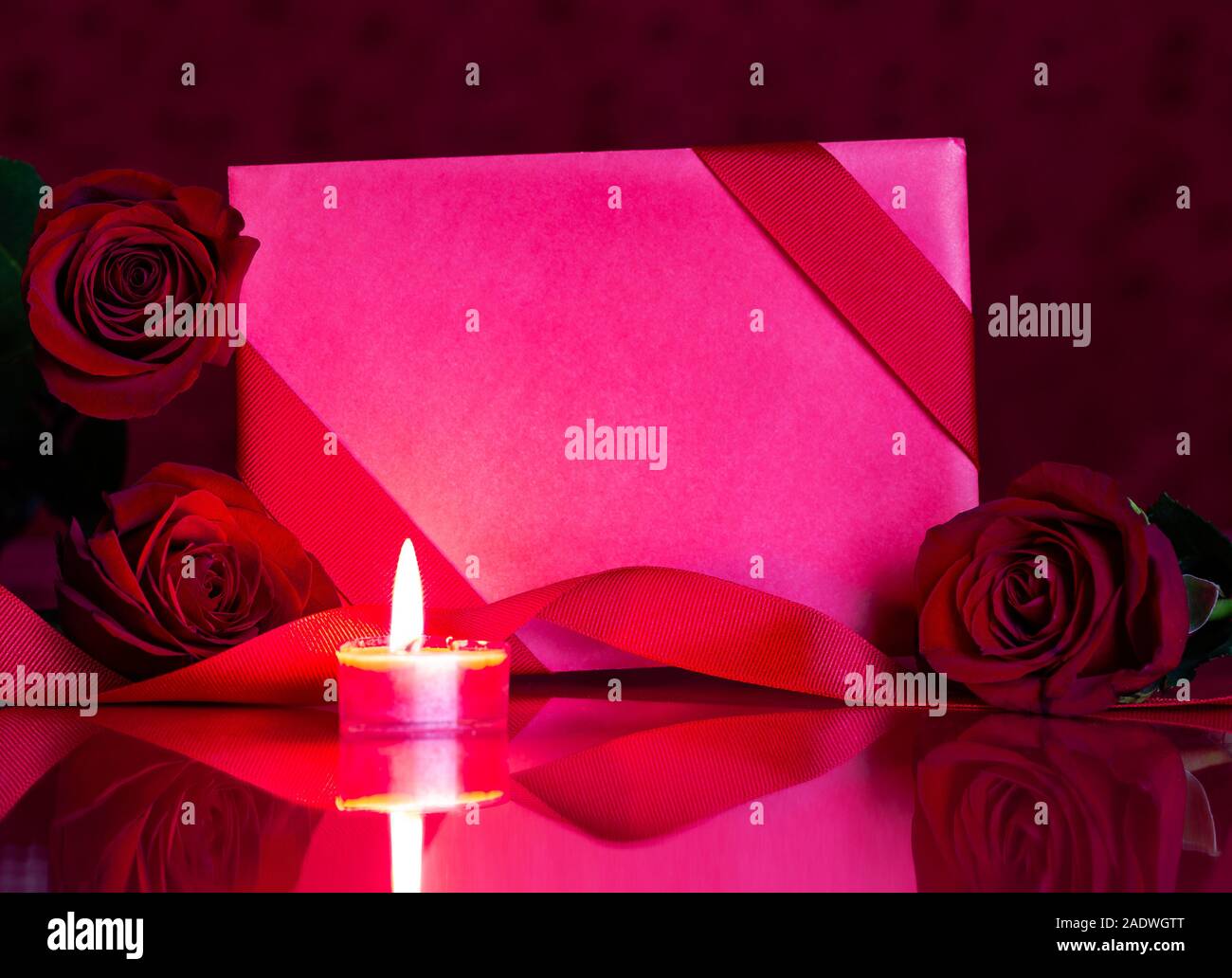 Closeup of a blank Valentine card and red roses with burning candle on a reflective tabletop Stock Photo
