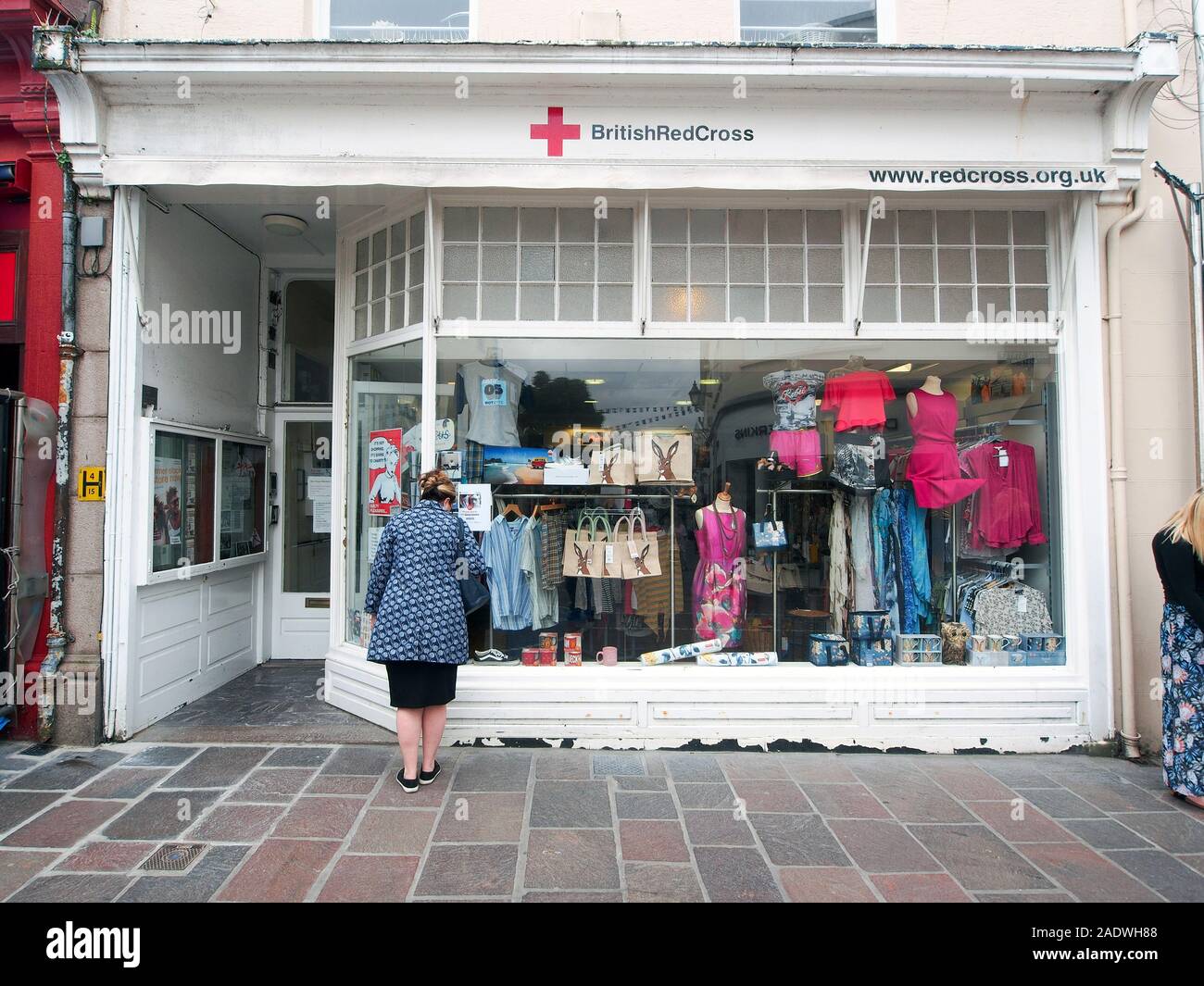 A woman looks into the window of a British Red Cross in Jersey, Channels Islands, UK Stock Photo -