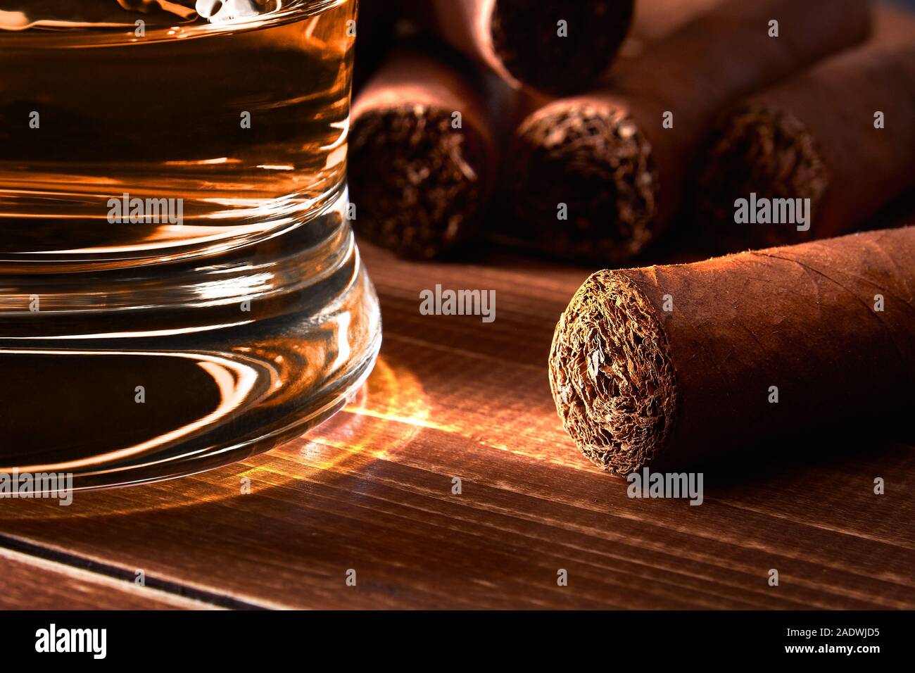 Still life with glass of whiskey or rum, cigar on old wooden board table. Blurred background. Stock Photo