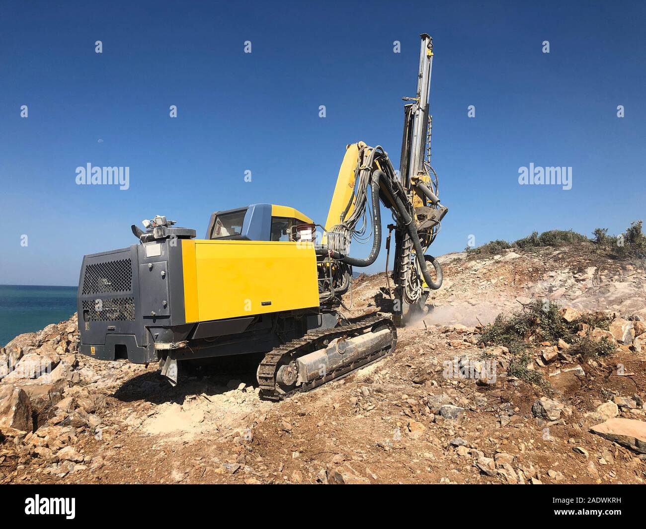 Yellow machinery is drilling holes on the top of rocky sea cliff during