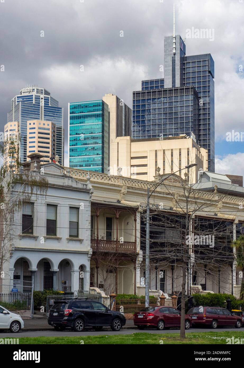 Vehicles parked in front of a row of terrace houses on Drummond St Carlton and  CBD office towers and skyscrapers in background Melbourne Australia. Stock Photo