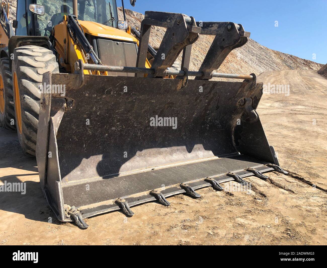 Bucket of yellow loader backhoe digging a trench during road