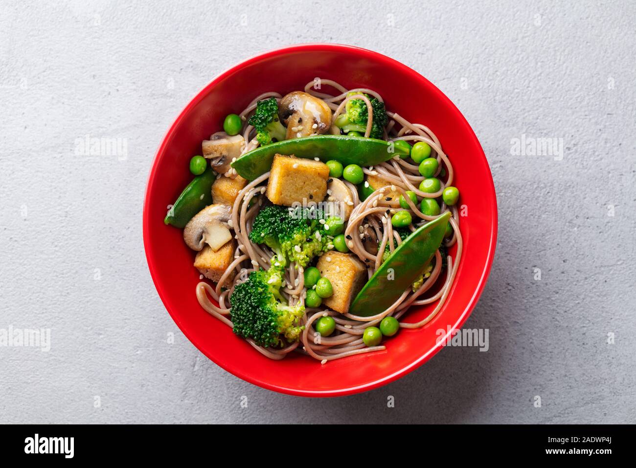 Soba noodles with vegetables and fried tofu in a bowl. Grey background
