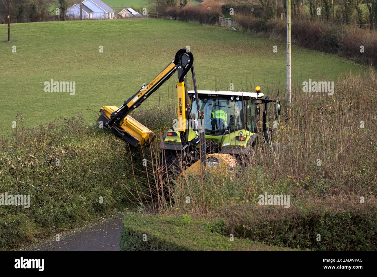 Aberystwyth Ceredigion Wales/UK December 04 2019: Yellow Tractor hedge cutting on a rural country lane, Stock Photo