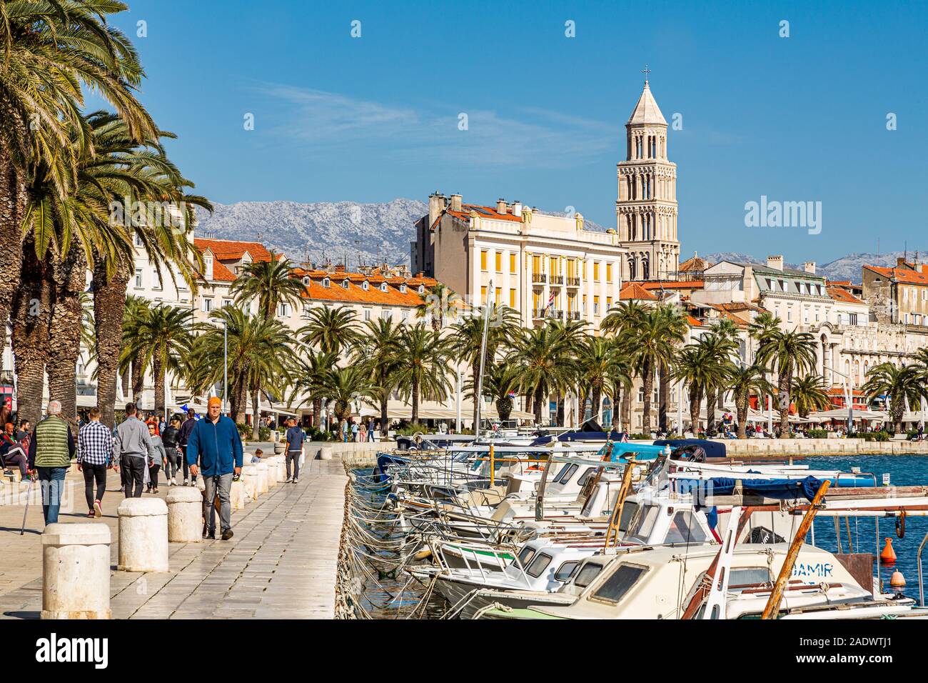 Panorama of people walking along the sunny waterside Riva promenade with the Cathedral of Saint Domnius, against blue sky, Split, Croatia Europe Stock Photo