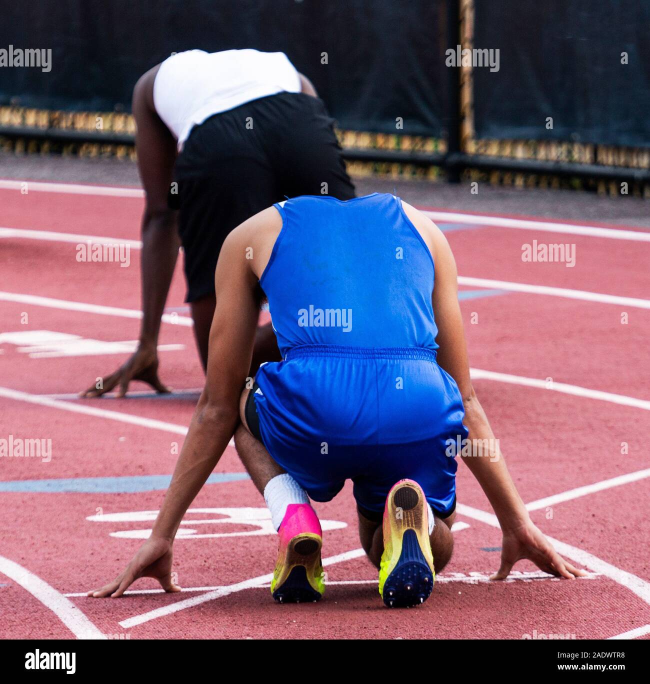 Two male high school sprinters are ready to sprint in lanes three and four during a track and field competition. Stock Photo