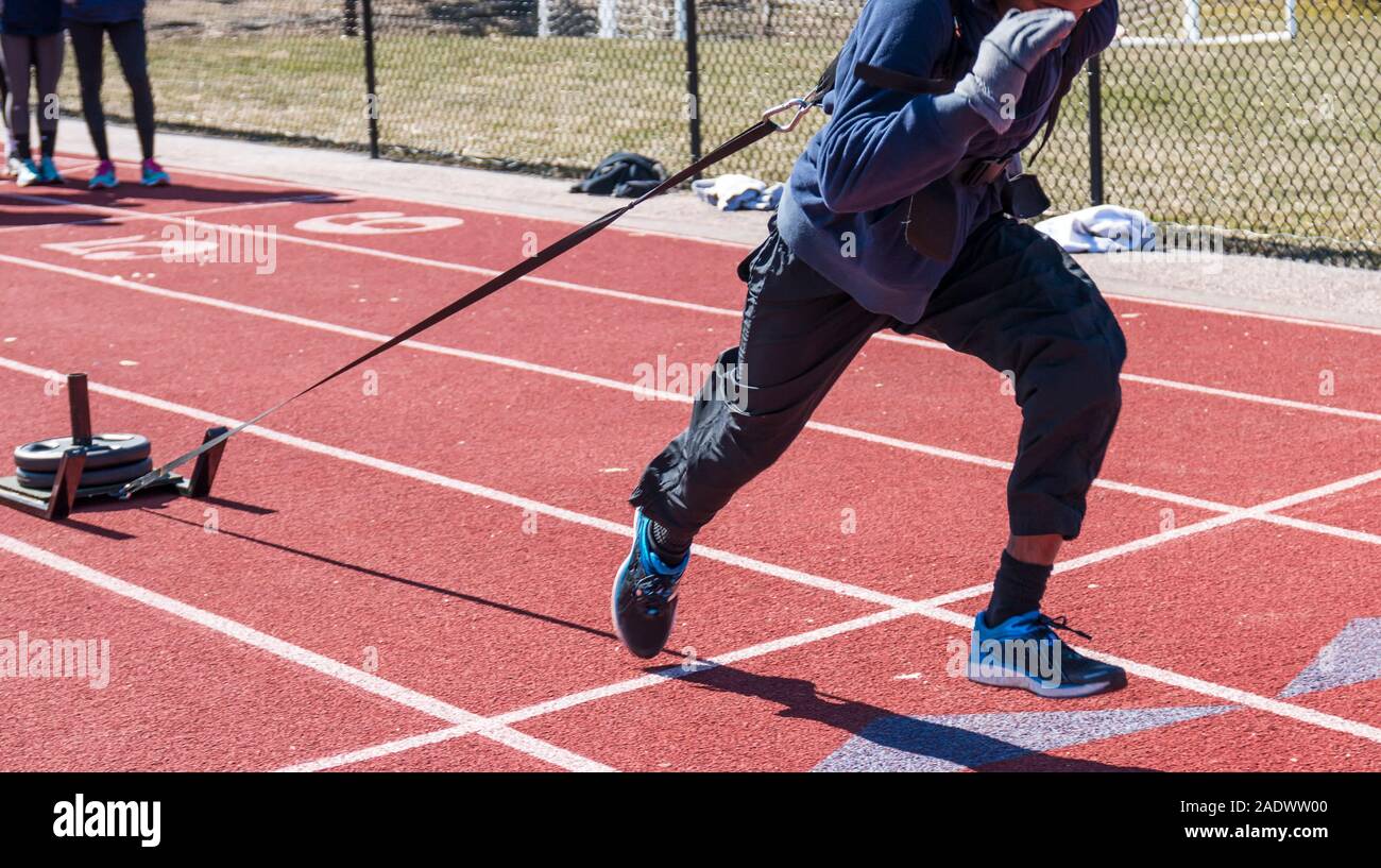 A high school male athlete is pulling a sled with 75 pounds of weight on it during speed and resistance training at track and field practice. Stock Photo