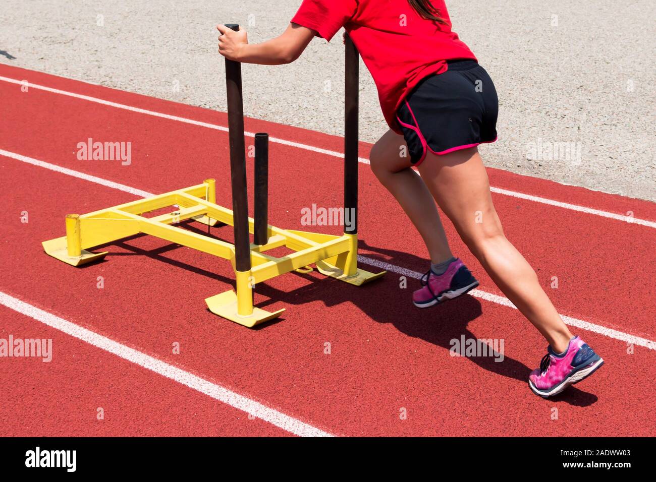 A female track and field athlete pushing a yellow sled down the track
