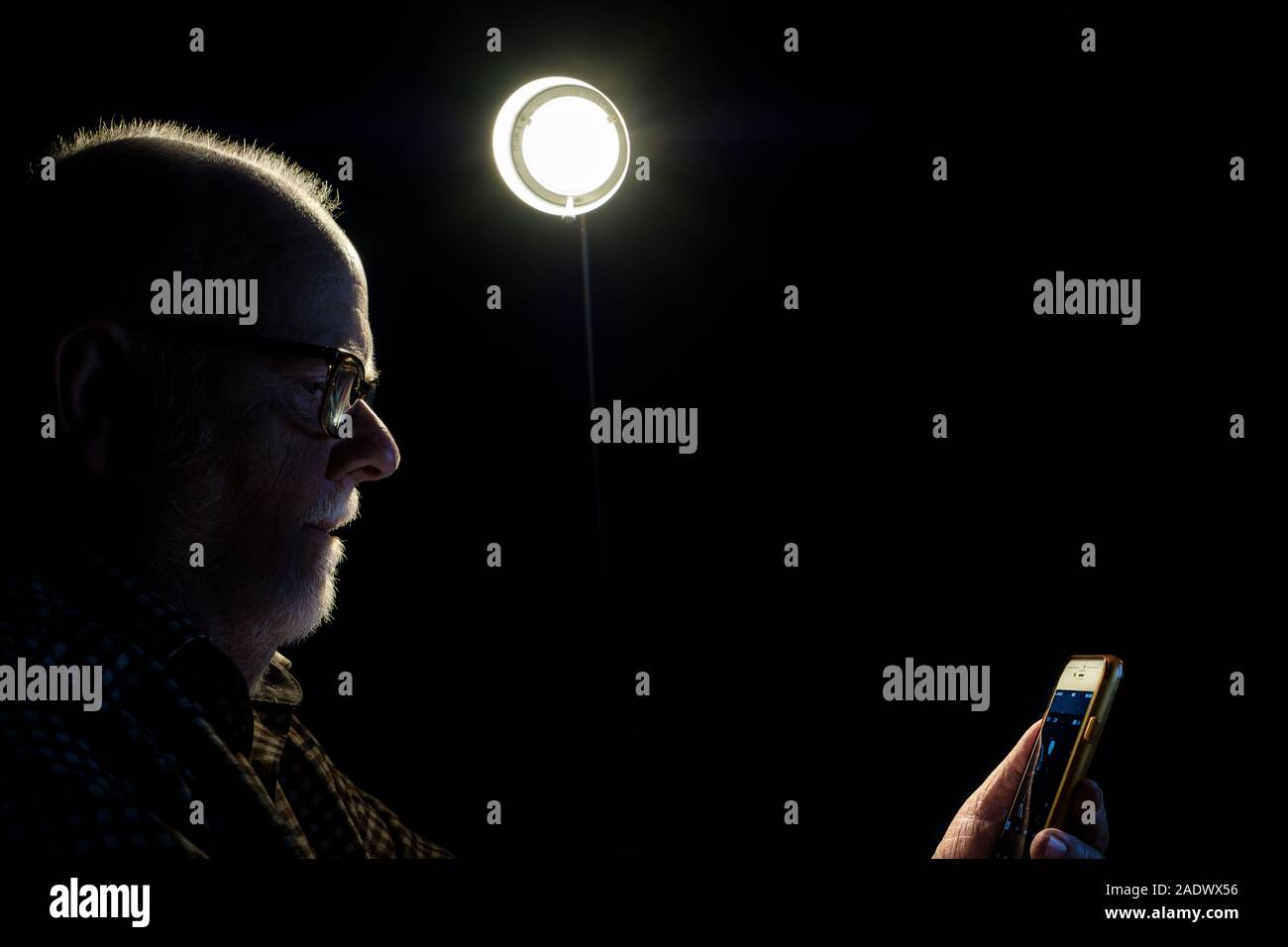 A man with a smartphone sitting under a bright light. Stock Photo