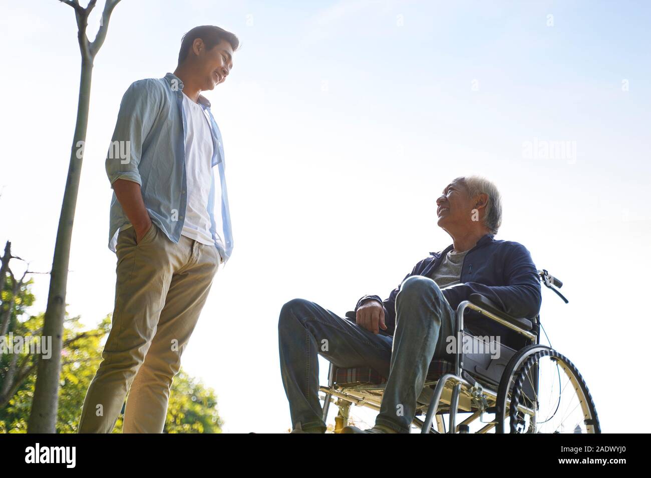 young asian adult man talking to wheelchair bound father, happy and smiling Stock Photo