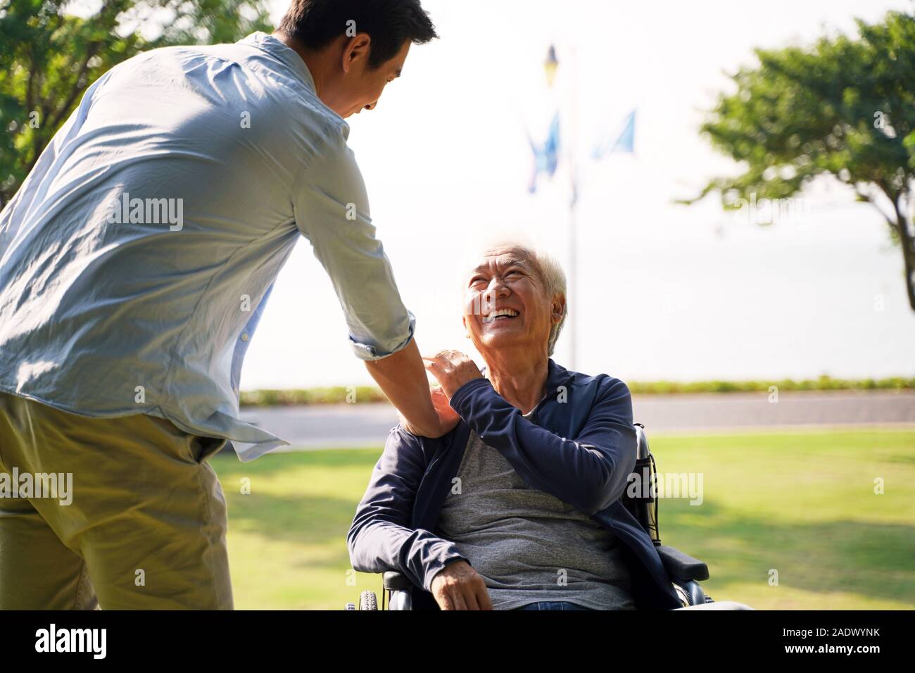 young asian adult son visiting father in nursing home giving dad a pat on the shoulder Stock Photo