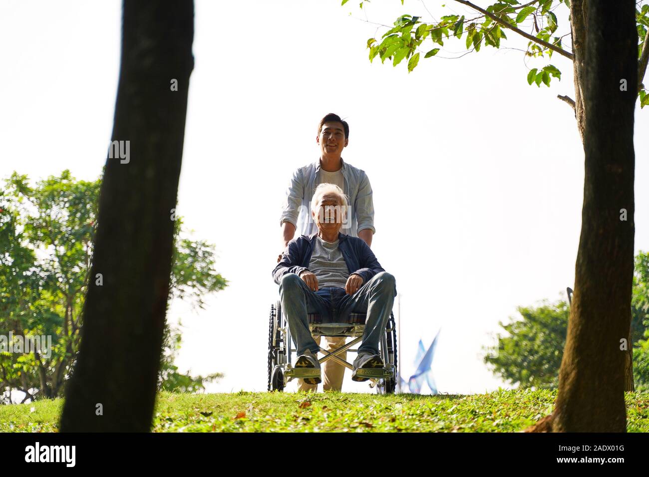 young asian adult son and wheelchair bound father enjoying nature in park Stock Photo