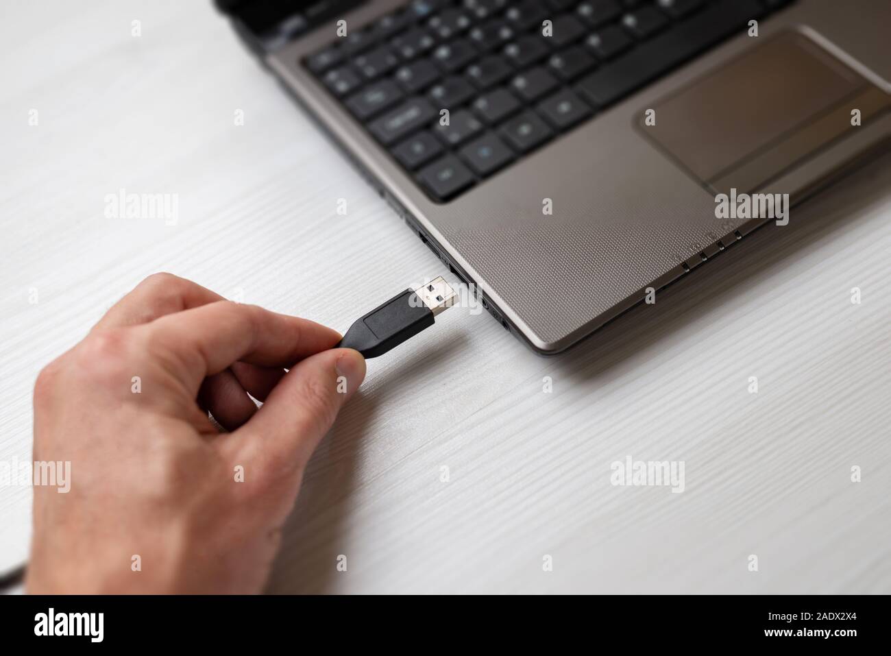 Hand holding usb cable and plugs it into the usb port on the laptop computer close-up Stock Photo