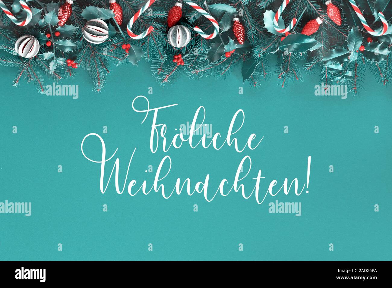 Text "Frohliche Weihnachten" in German that means "Happy Christmas". Xmas flat lay on green paper with red decorations. Natural fir and holly twigs de Stock Photo