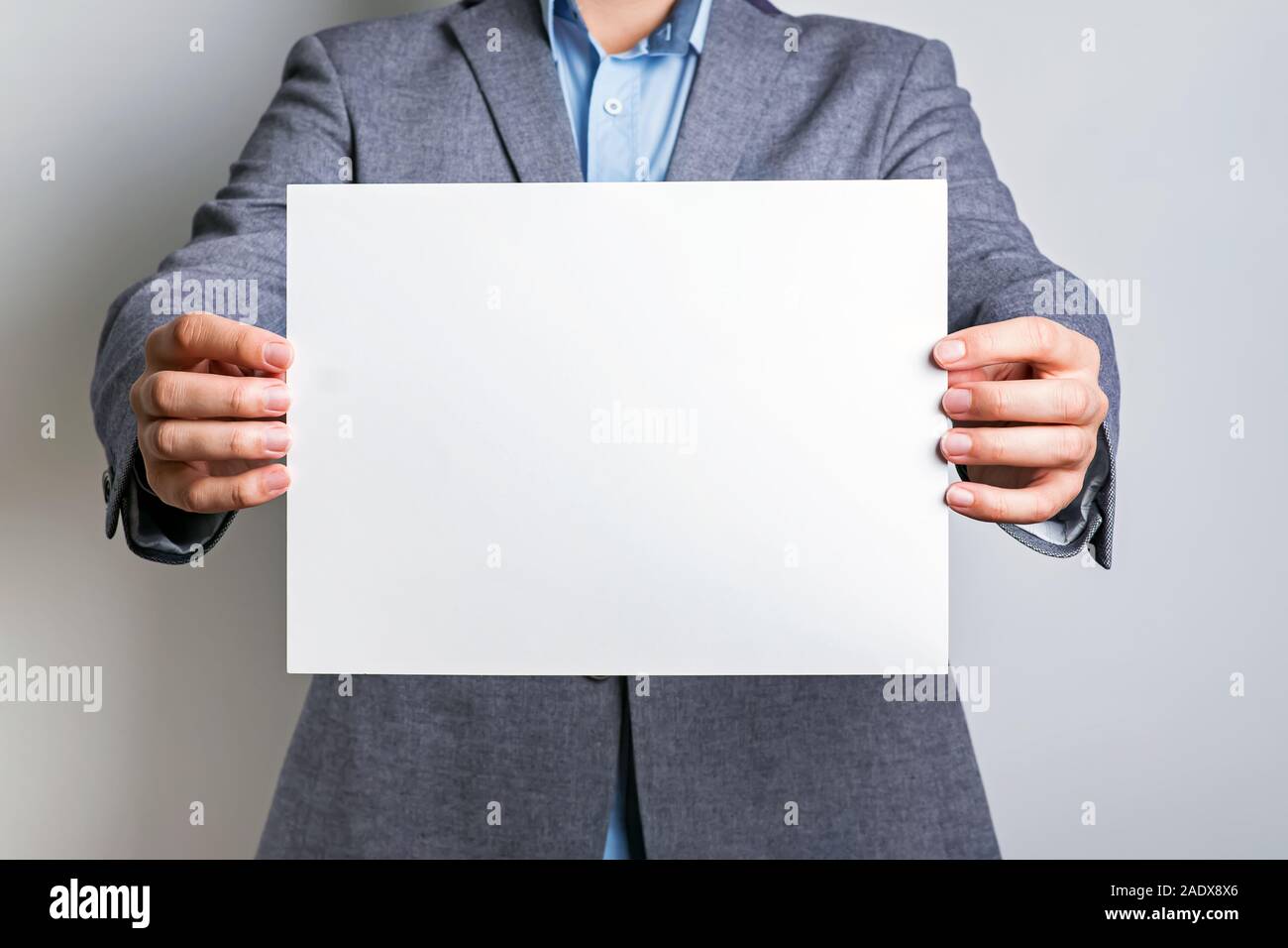 Unrecognisable man in grey suit holding a blank white board Stock Photo