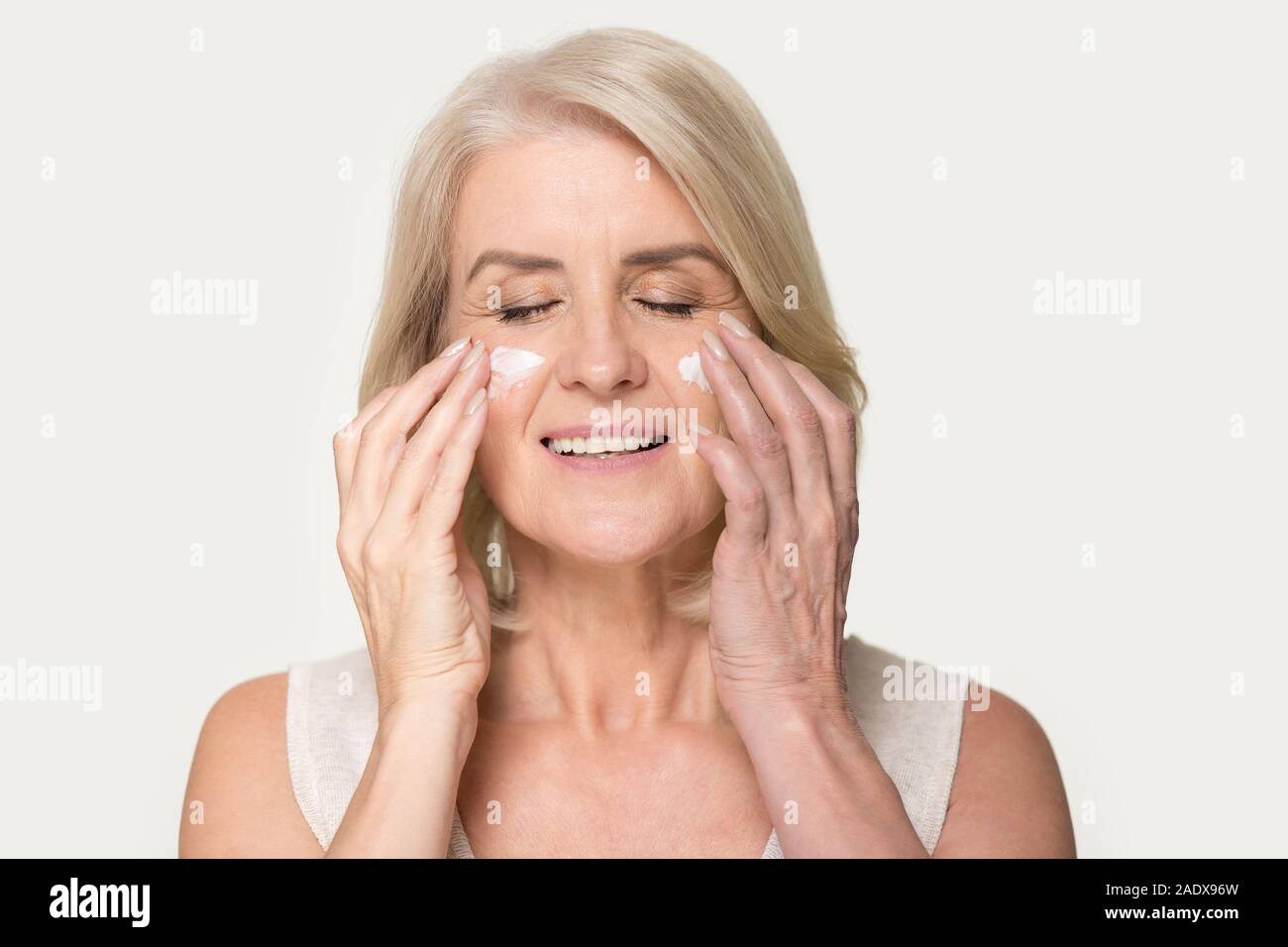 Smiling mature woman applying rejuvenating cream on her face skin Stock Photo