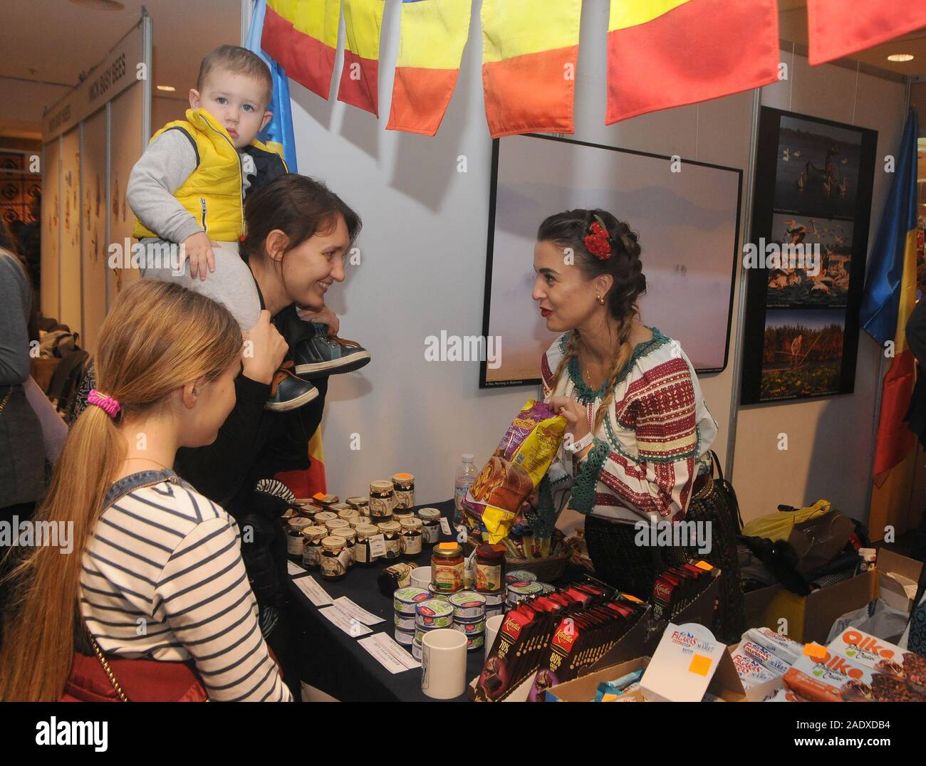 A woman and a kid at the Embassy of Rumunia counter during the event at the NSC Olimpiysky.The 27th annual Charity Fair “IWCK Charity Bazaar”, a special event where representatives of 49 embassies of foreign countries organise an exhibition and sale of various national products. Stock Photo