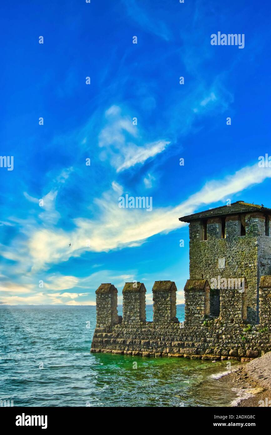 Vertical photo of water castle on coast of famous italian Lago di Garda. Castle is in small town Sirmione. Sky is blue with dramatic clouds. Stock Photo