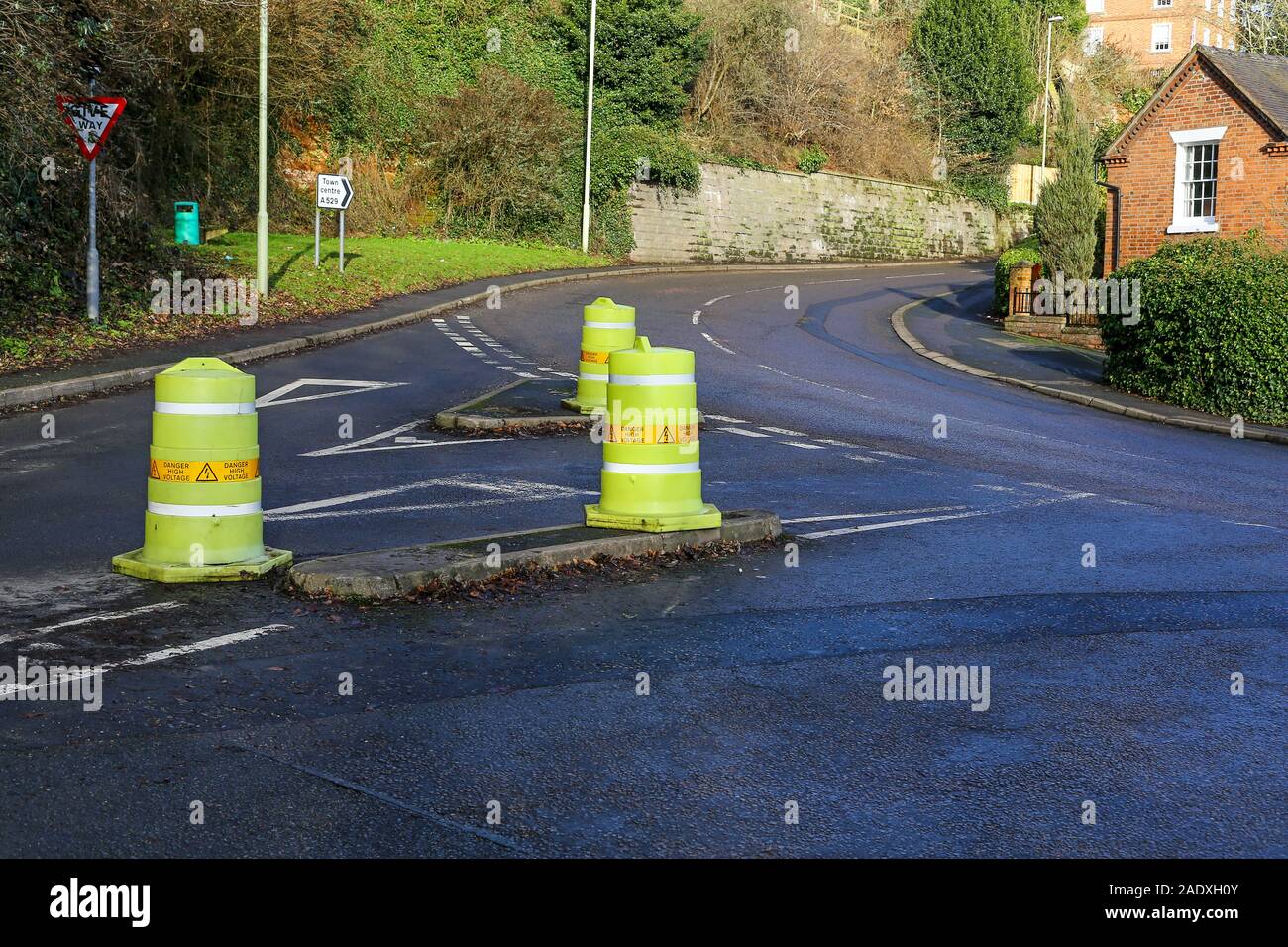 Traffic cones or bollards with 'danger high voltage' written on them on a traffic island near a road junction, England, UK Stock Photo