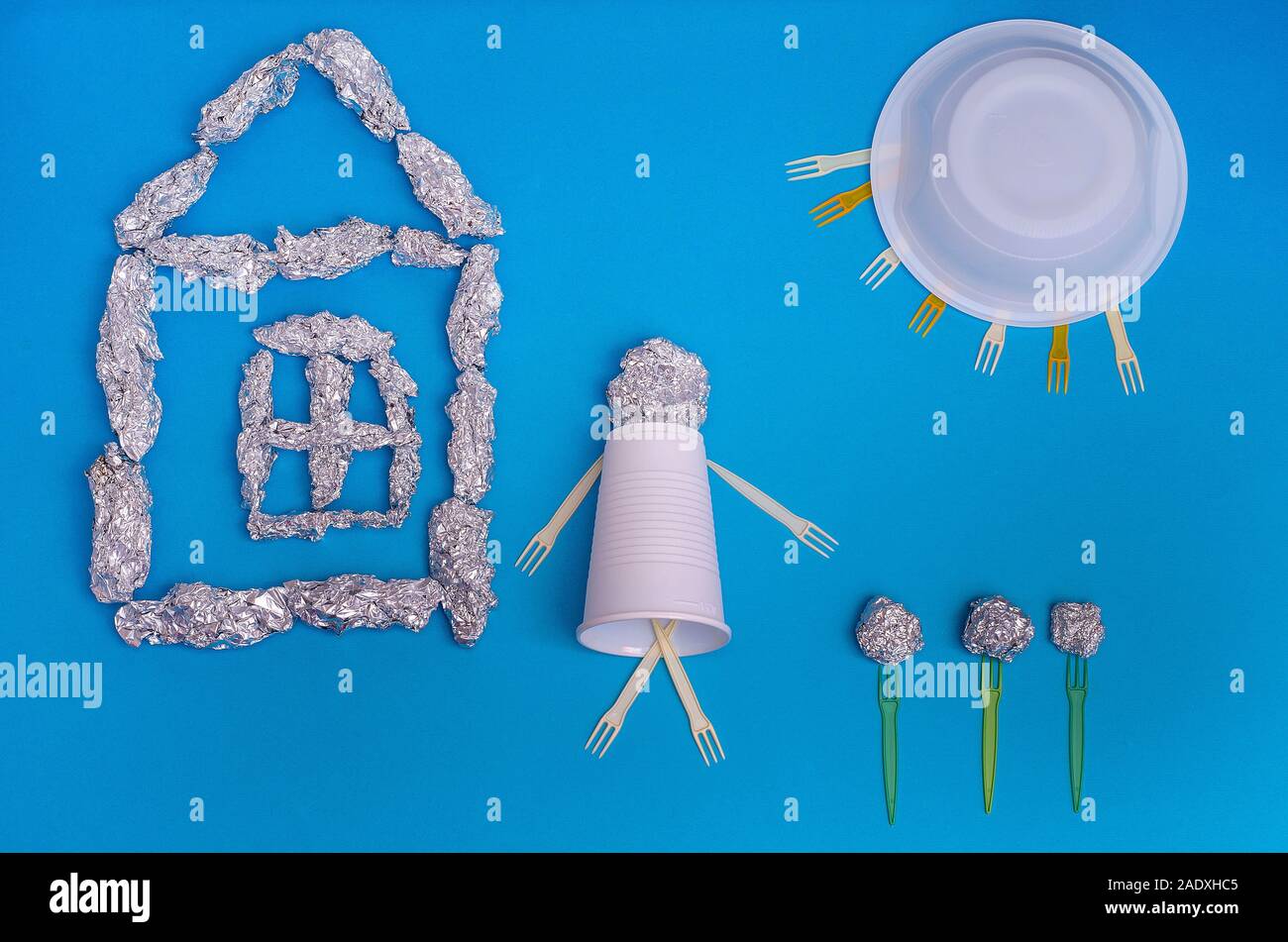 Concept: ecology, environmental pollution. A world out of garbage: a house, a man, the sun, flowers made of foil and plastic on a blue background. Rec Stock Photo