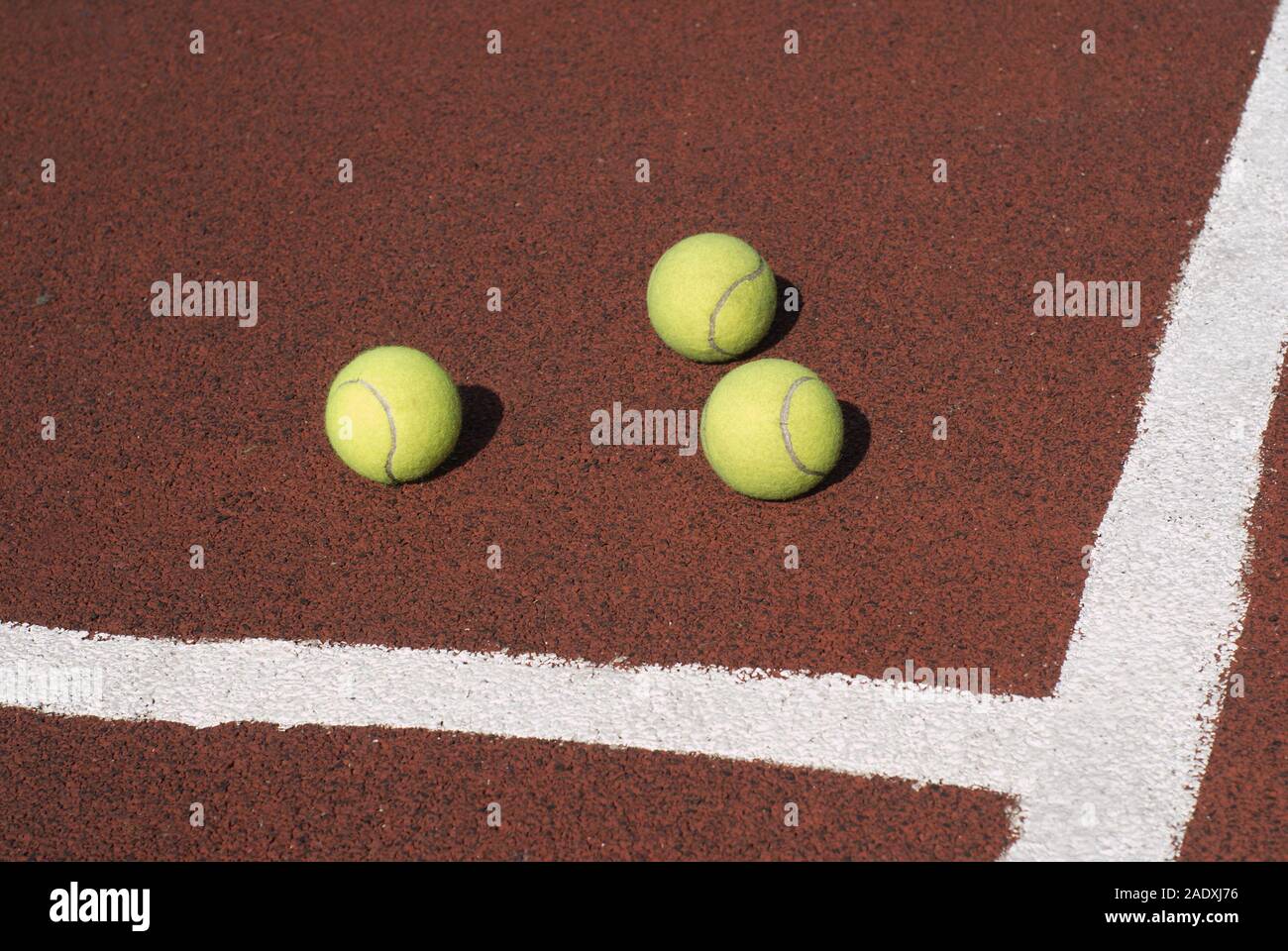 Three tennis balls on brown synthetic court outdoors top view Stock Photo
