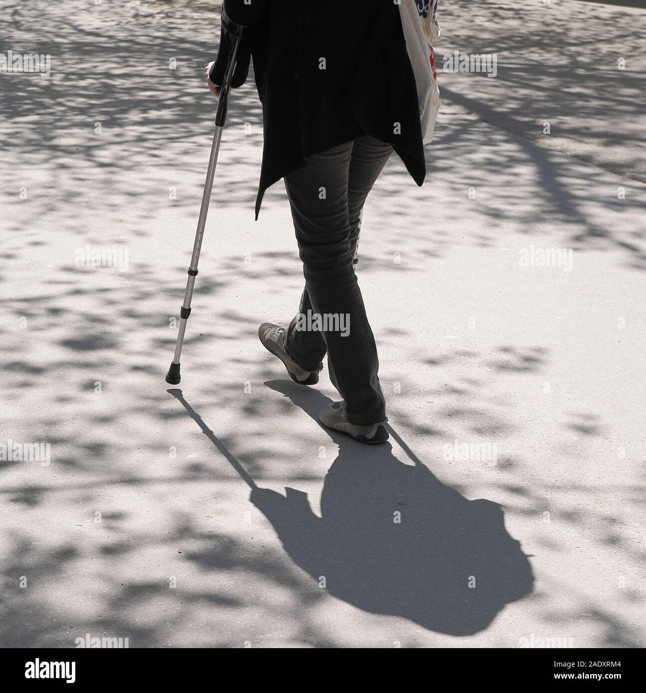 One person with crutch walking on concrete with tree shadows. Retirement,  health and insurance concept Stock Photo - Alamy