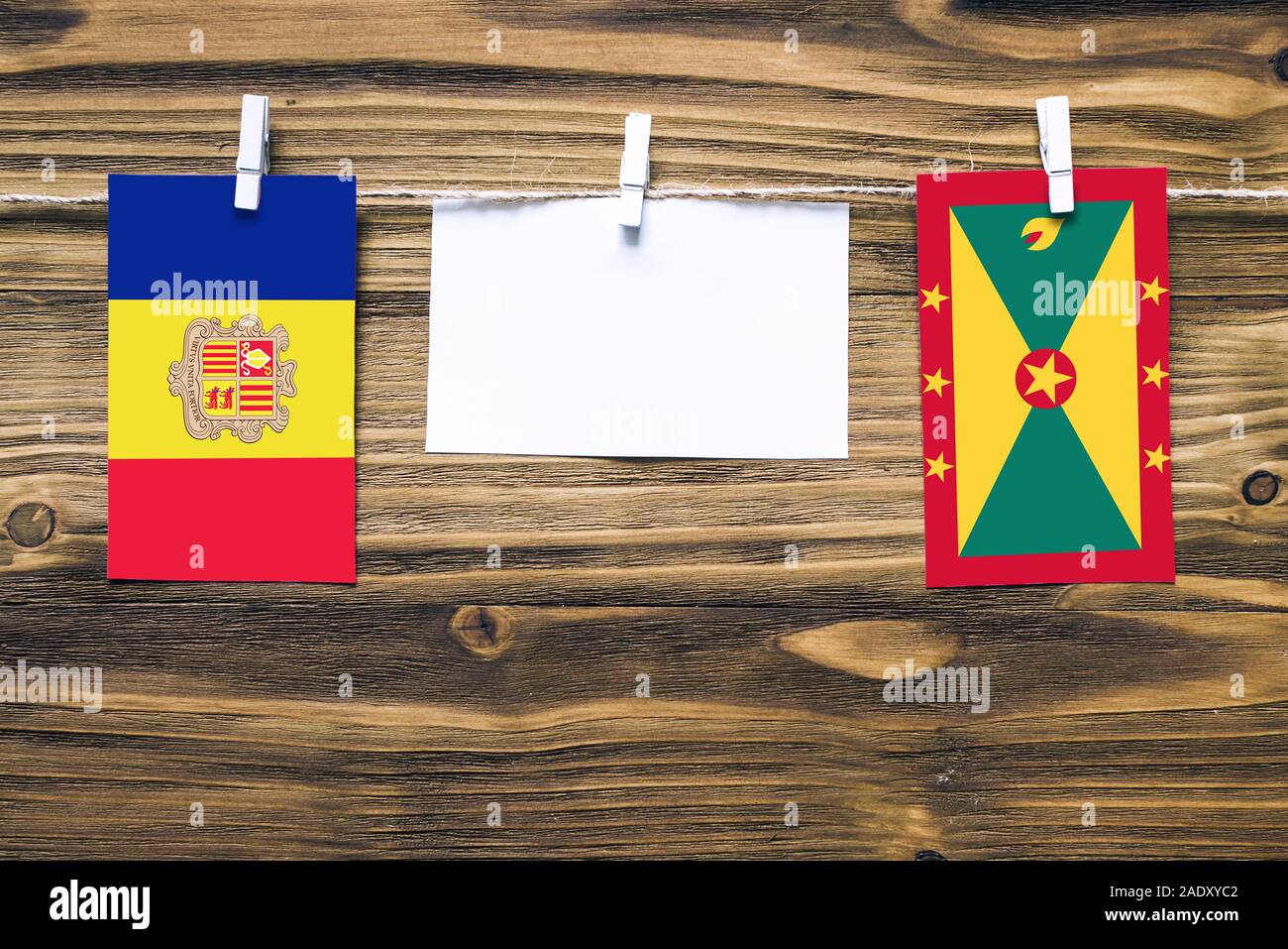 Hanging flags of Andorra and Grenada attached to rope with clothes pins with copy space on white note paper on wooden background.Diplomatic relations Stock Photo