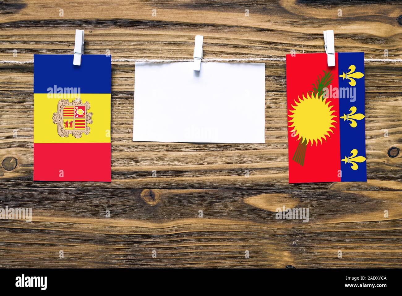 Hanging flags of Andorra and Guadeloupe attached to rope with clothes pins with copy space on white note paper on wooden background.Diplomatic relatio Stock Photo