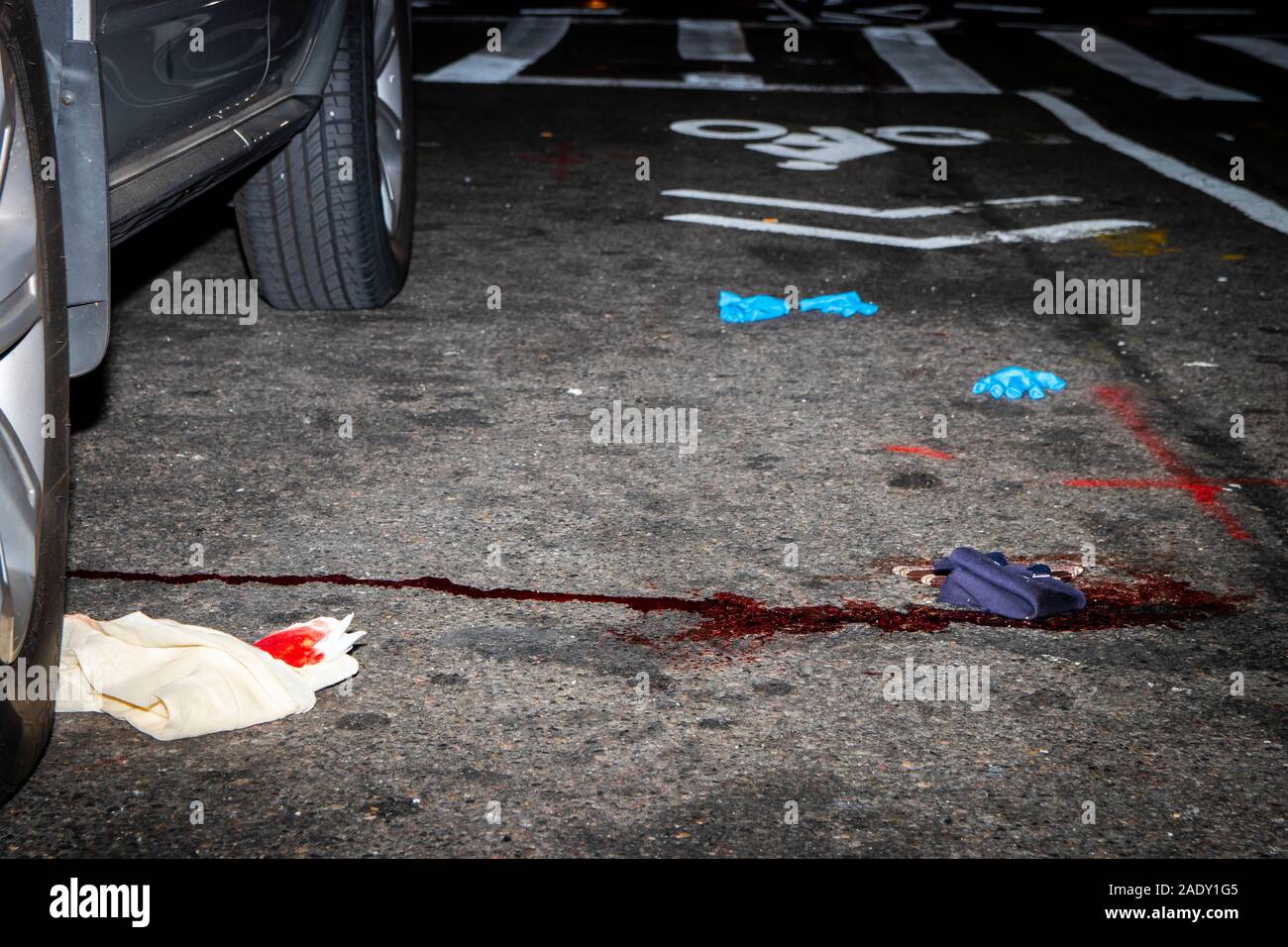 Blood stains on the street in New York City, next to discarded latex gloves and blood soaked rags Stock Photo