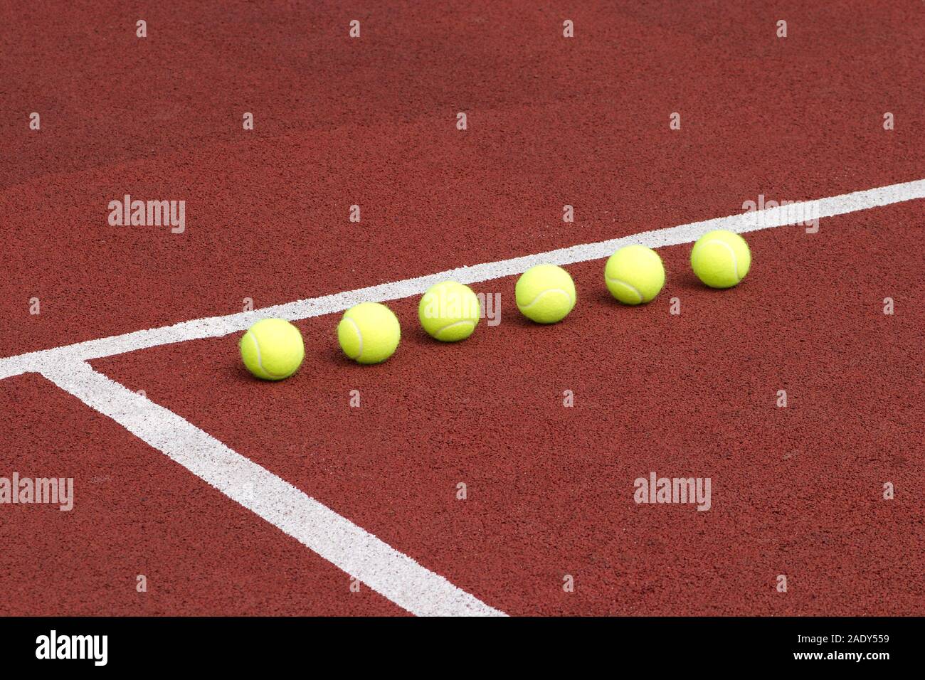 Line of six yellow tennis balls on red synthetic court side view Stock Photo