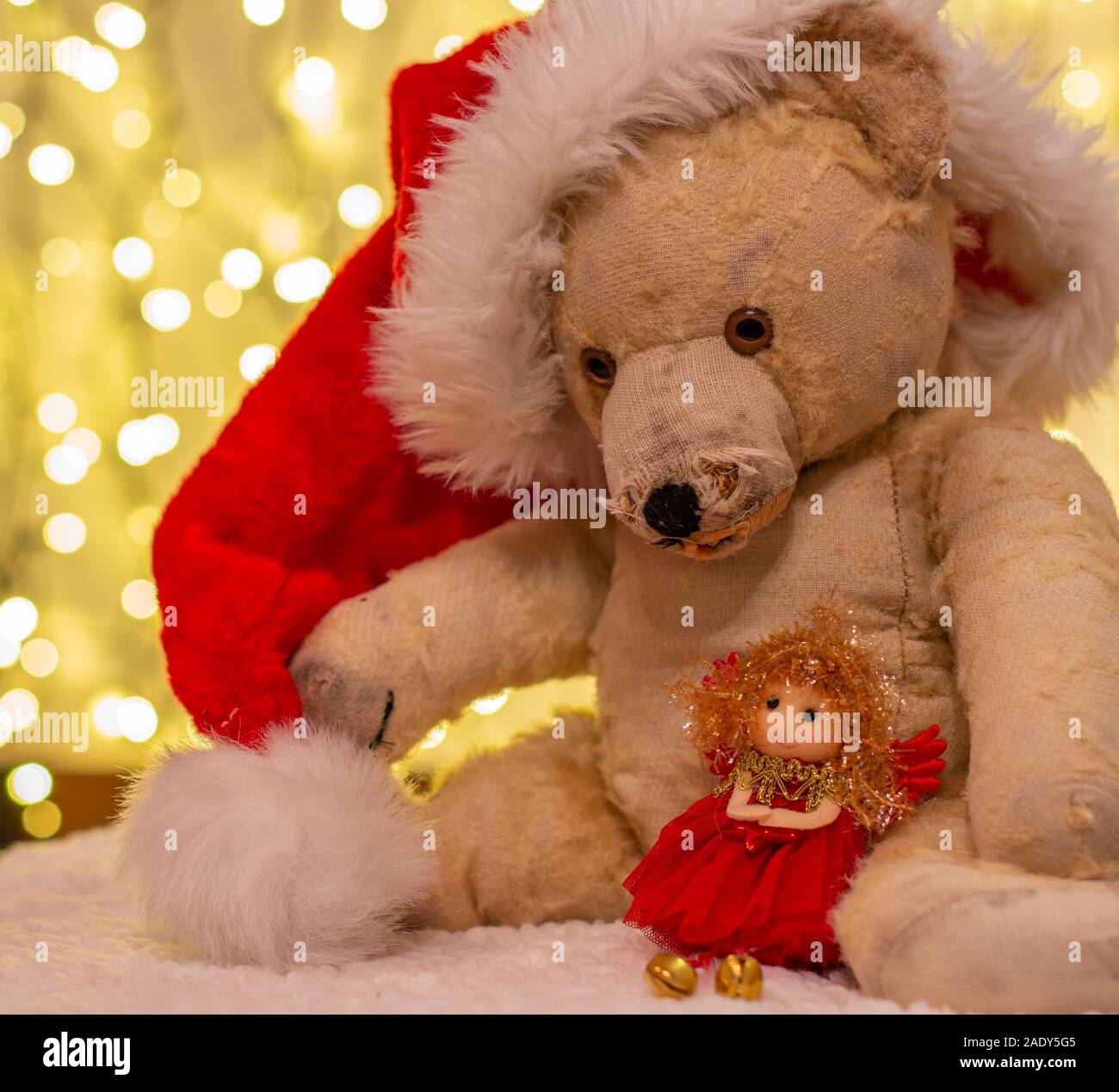 Very old soft toy. Old teddy bear with red  Christmas hat. In the backdrop are christmas lights. With soft doll in red. Stock Photo