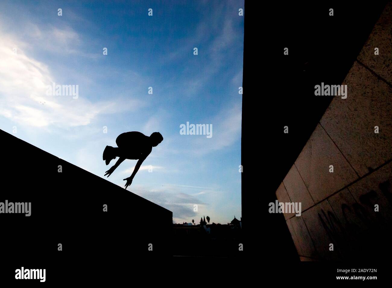 Young man practicing parkour in the street with a blue sky and backlight Stock Photo