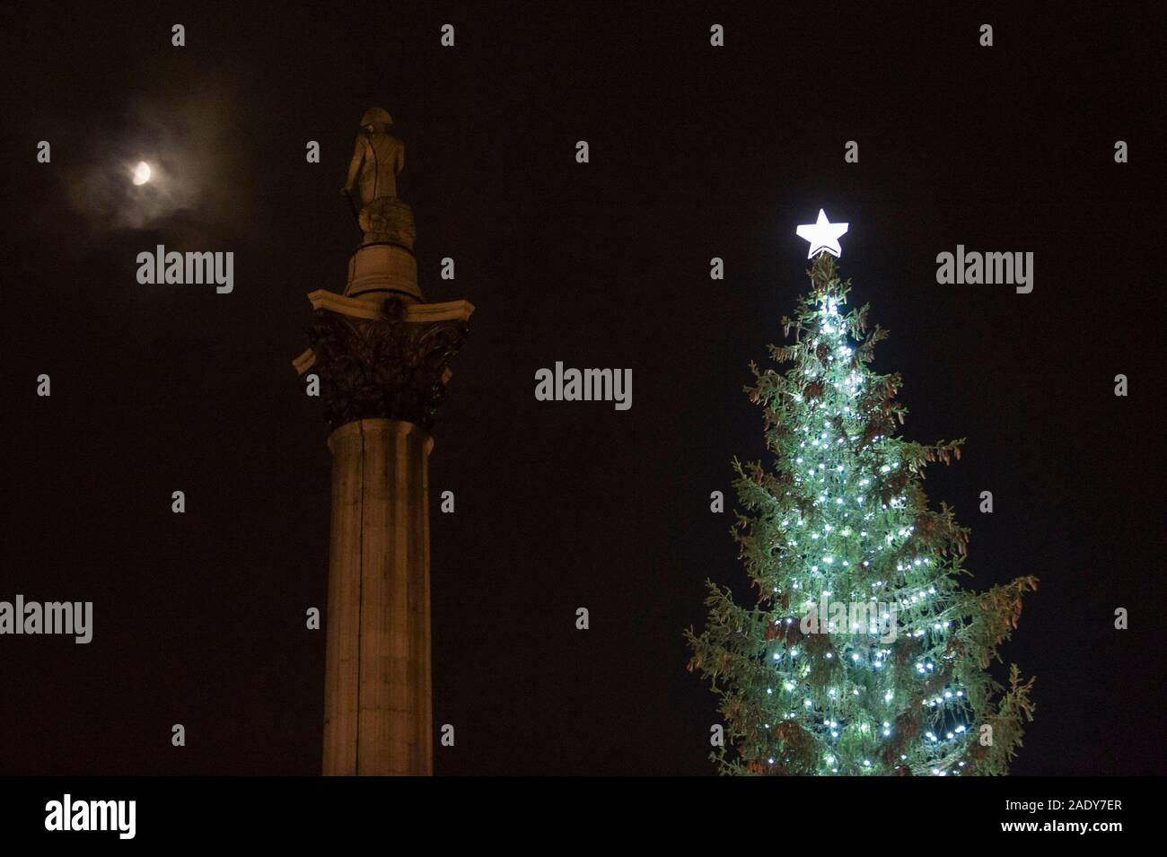 London, UK.  5 December 2019.  The moon, Nelson's Column and the newly lit Christmas Tree in Trafalgar Square.  The tree, a Norwegian spruce, is donated by the City of Oslo to the people of London each year as a token of gratitude for Britain’s support during the Second World War.  This year, the tree has been criticised for having branches which look too sparse. Credit: Stephen Chung / Alamy Live News Stock Photo