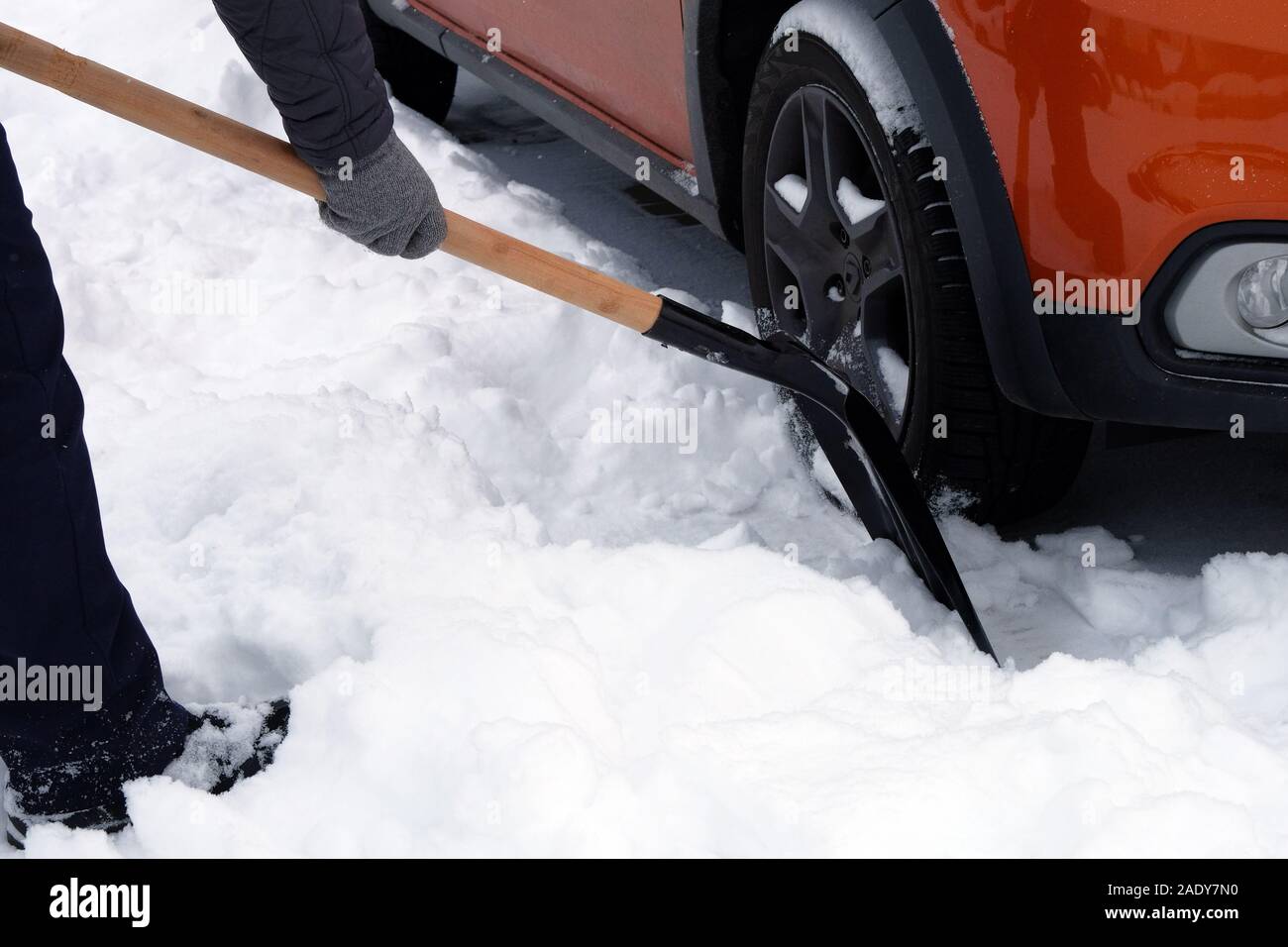 Man with shovel is brushing snow around car after snow storm. Shovel in hand. Winter problems of car drivers. Stock Photo